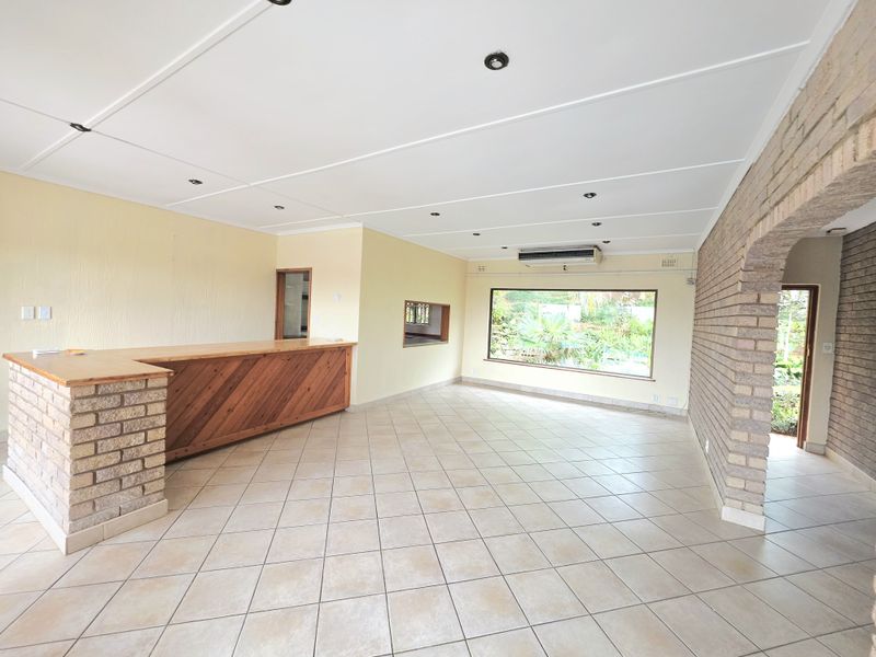 Spacious living area featuring a built-in bar, exposed brick archway, tiled flooring, and large window providing natural light and garden views.