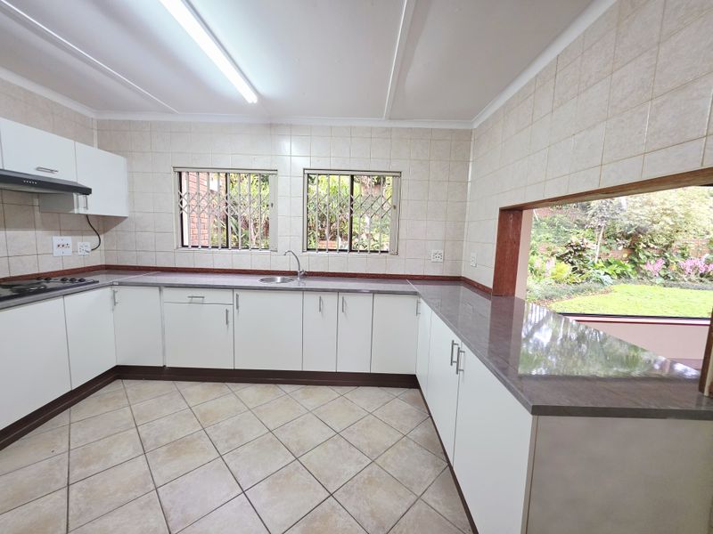 A clean, functional kitchen featuring white cabinetry, stone countertops, tiled flooring, and a convenient serving hatch overlooking the garden.