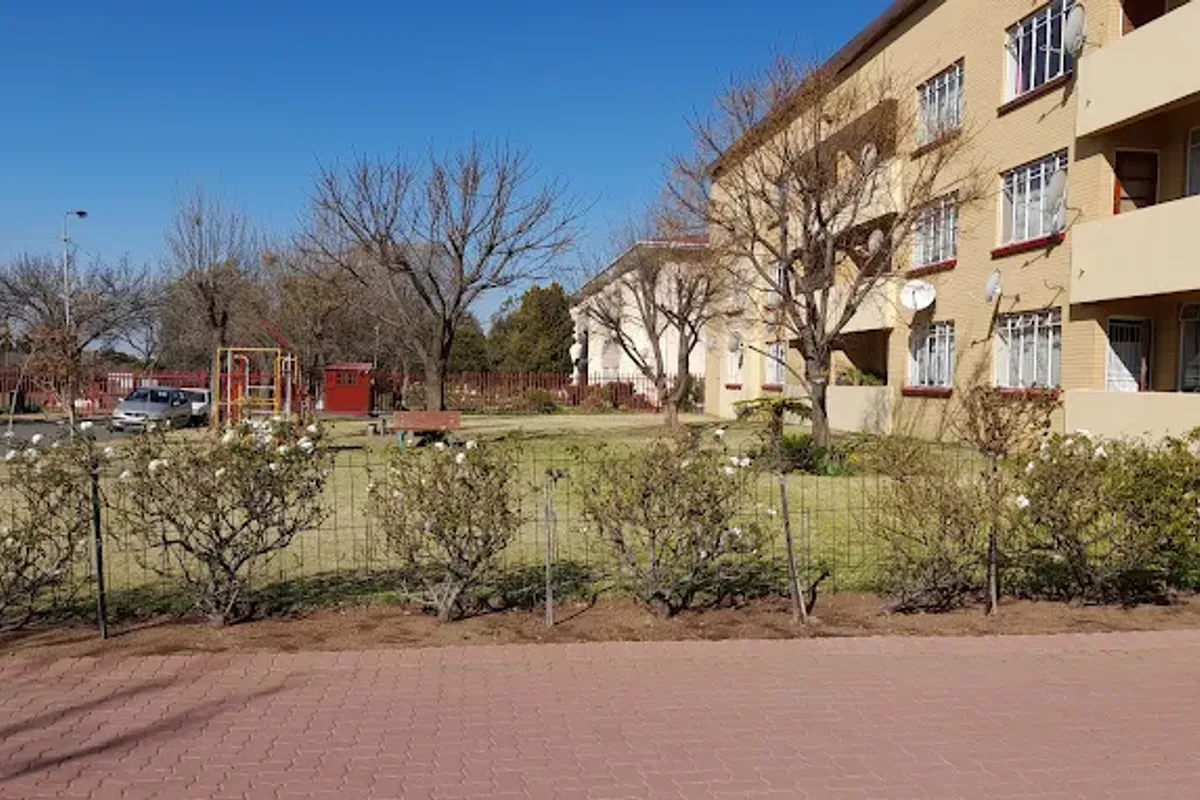 A view of the apartment building exterior featuring a brick facade, private balconies, and a shared garden area with paved walkways.