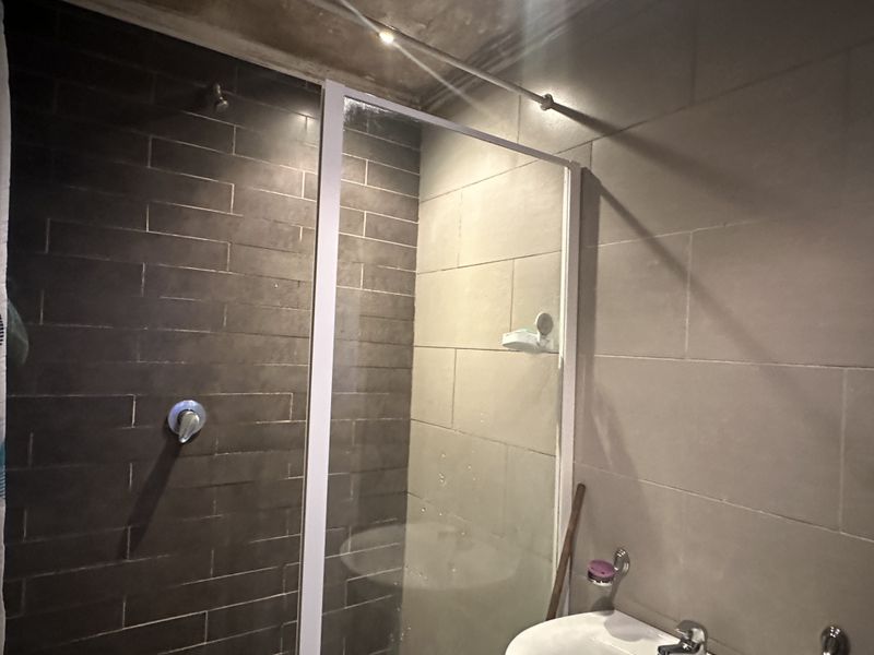 A functional bathroom featuring a glass-enclosed shower with dark tiled accents and a standard basin with mixer tap.