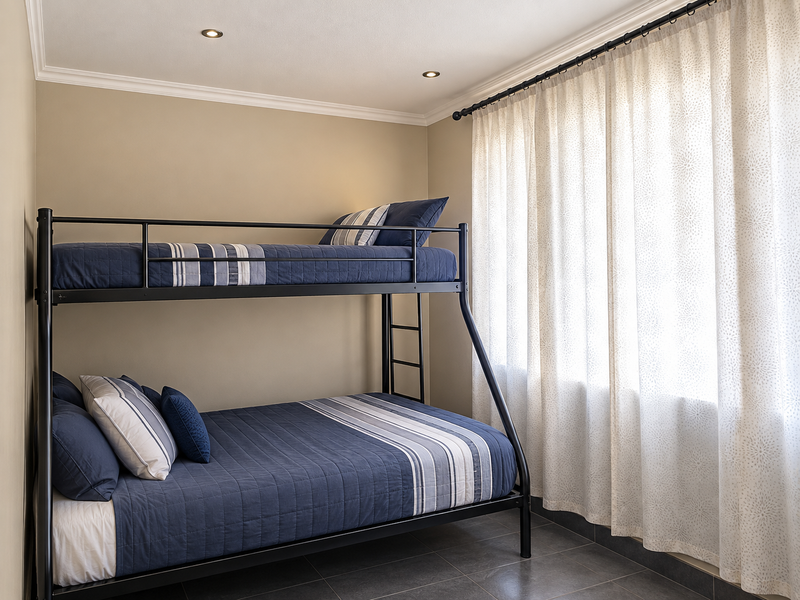 A well-maintained bedroom featuring neutral wall tones, recessed downlighting, decorative cornice, and tiled flooring, offering a clean and functional living space.