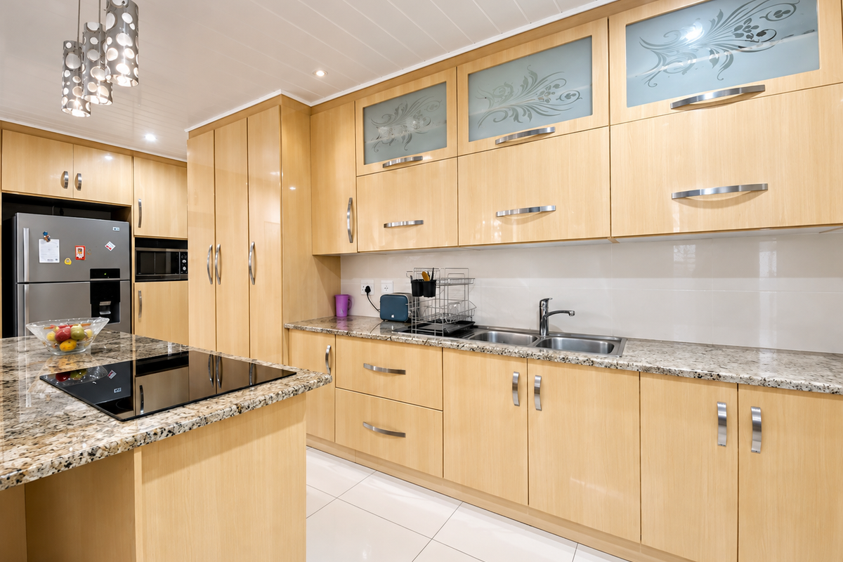 Modern kitchen featuring light wood cabinetry, granite countertops, integrated appliances, and a central island with a glass-top hob.