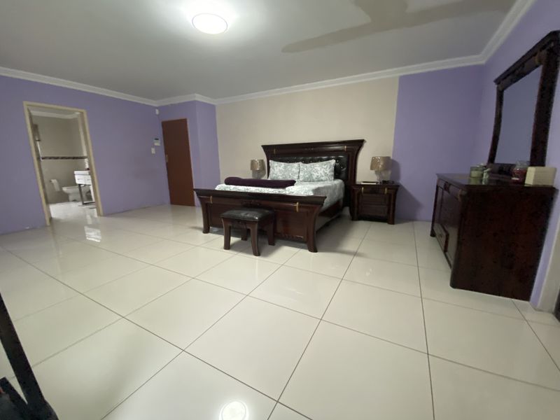 Spacious bedroom featuring large format floor tiles, cove cornicing, and an adjoining en-suite bathroom.
