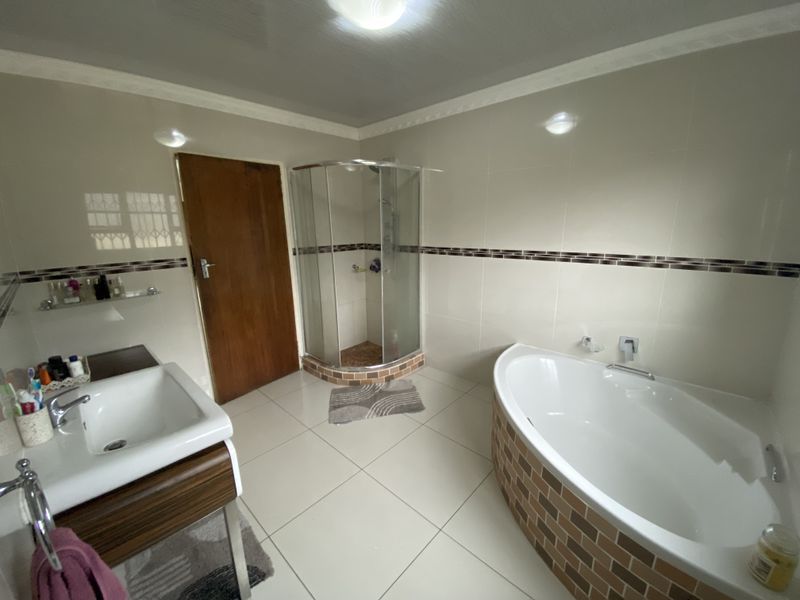 A well-maintained bathroom featuring a corner shower enclosure, a curved bathtub with brick-style tiling, and a modern vanity basin.
