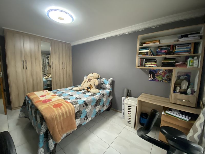 A bedroom featuring built-in wooden wardrobes, a built-in desk with shelving, and tiled flooring. The room includes a ceiling cornice and neutral wall finishes.