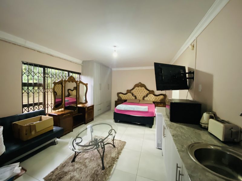 A spacious bedroom featuring built-in cupboards, a small kitchenette area with a sink, and security gates on the windows.