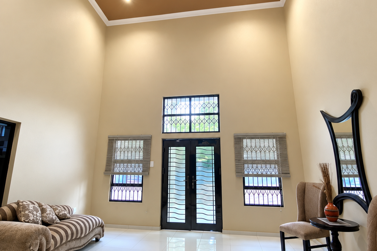 Spacious living area featuring double volume ceilings with a recessed tray design, tiled flooring, and secure entrance doors with integrated security bars.