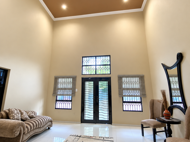Spacious living area featuring double volume ceilings with a recessed tray design, tiled flooring, and secure entrance doors with integrated security bars.