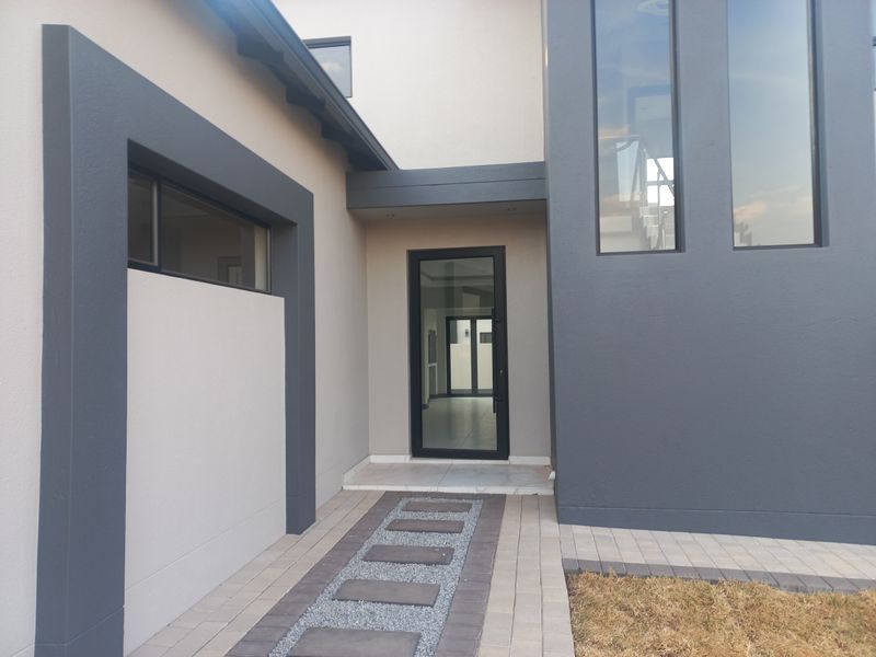 Modern front entrance featuring a sleek glass door, contemporary grey and cream facade, and a paved walkway with gravel accents.