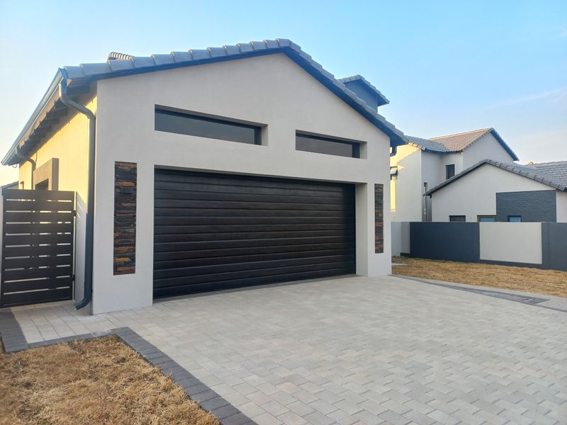Modern residential garage exterior featuring a dark sectional door, stone cladding accents, and a neatly paved driveway.