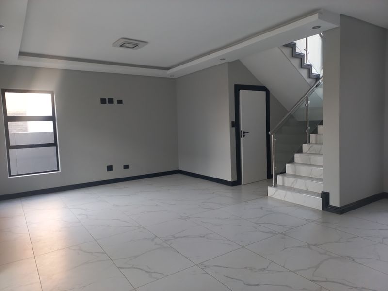 A bright, modern, and spacious open-plan living area featuring high-quality marble-look floor tiles and a contemporary staircase with a glass balustrade.