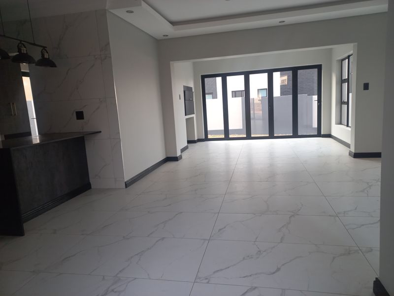 Spacious open-plan living area featuring modern marble-look floor tiles, recessed ceiling lights, a built-in fireplace, and large black aluminium stacker doors leading outdoors.