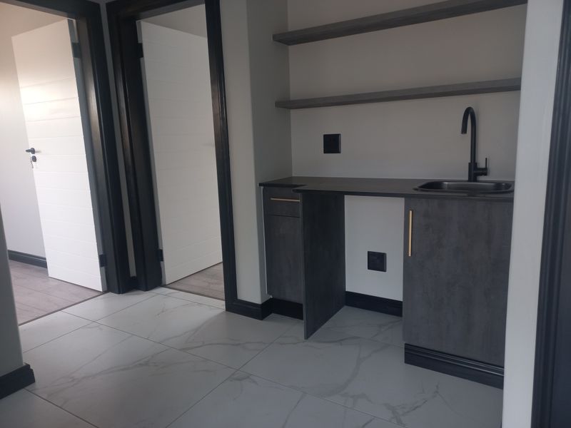 A modern, minimalist scullery or kitchenette area featuring dark cabinetry, a sleek sink, and floating shelves with contemporary finishes.