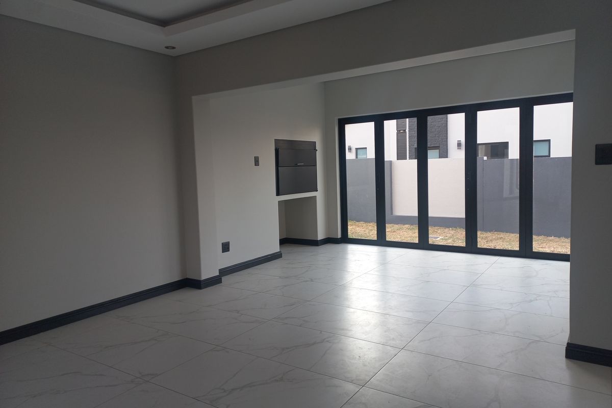 Spacious open-plan living area featuring modern tiled flooring, recessed ceiling lighting, and large aluminium stacker doors leading to the rear garden.
