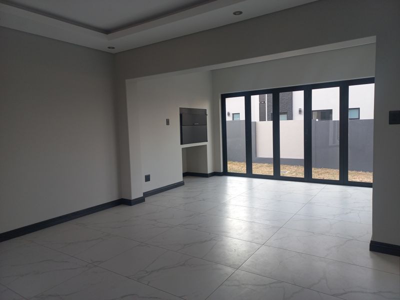 Spacious open-plan living area featuring modern tiled flooring, recessed ceiling lighting, and large aluminium stacker doors leading to the rear garden.
