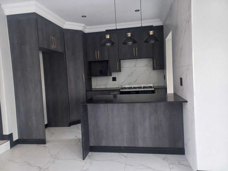 Modern kitchen featuring dark cabinetry, marble-look tile flooring, a central island, and a built-in gas hob with stylish pendant lighting.