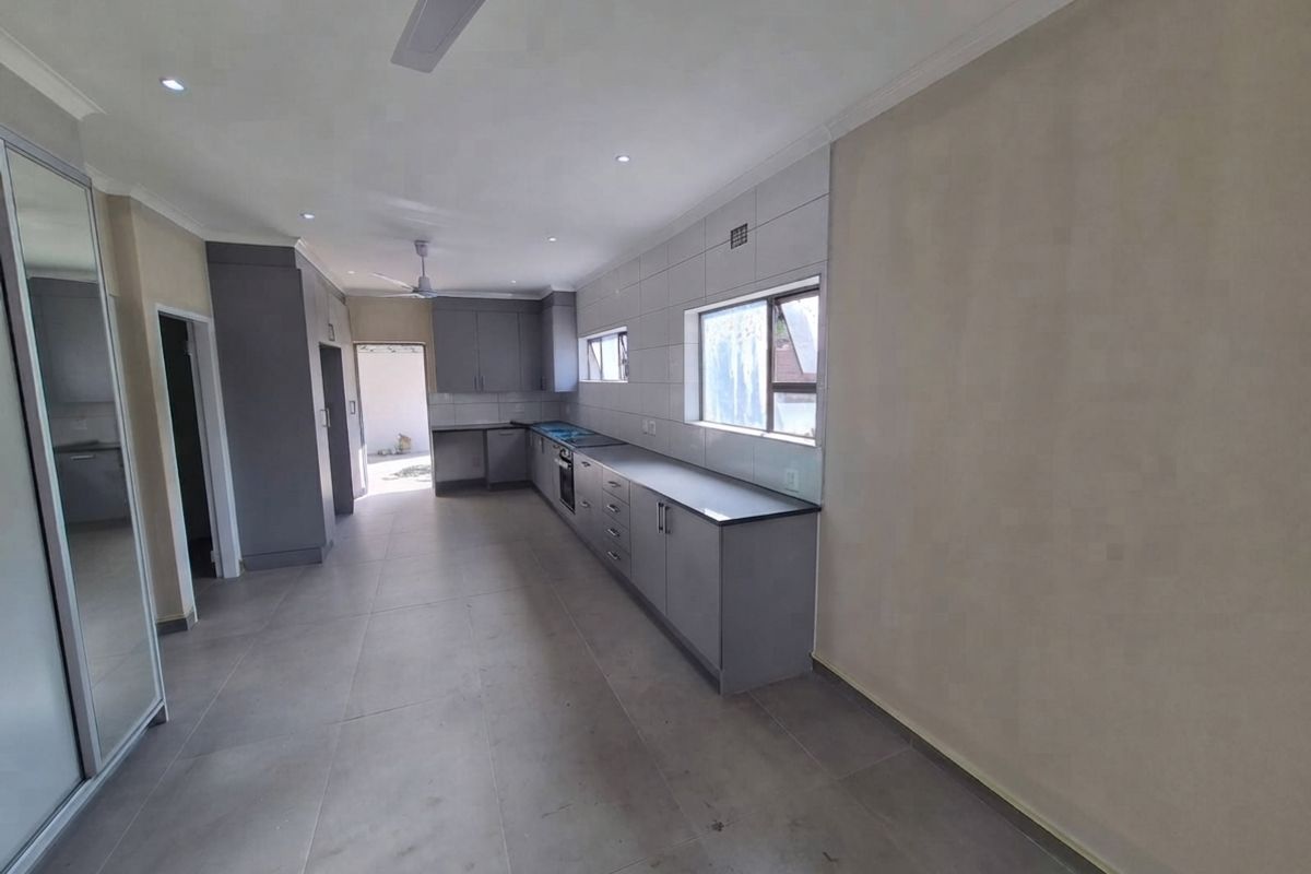 A modern, spacious kitchen featuring grey built-in cabinetry, tiled splashbacks, integrated appliances, and neutral floor tiles in an open-plan layout.