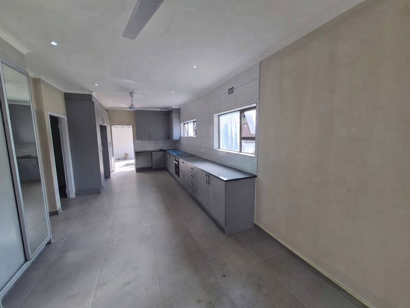 A modern, spacious kitchen featuring grey built-in cabinetry, tiled splashbacks, integrated appliances, and neutral floor tiles in an open-plan layout.