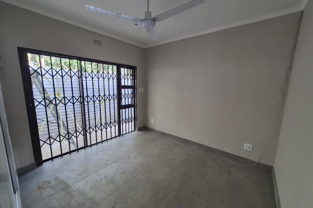 An empty living room featuring neutral walls, large format floor tiles, a ceiling fan, and a sliding door with a security gate.