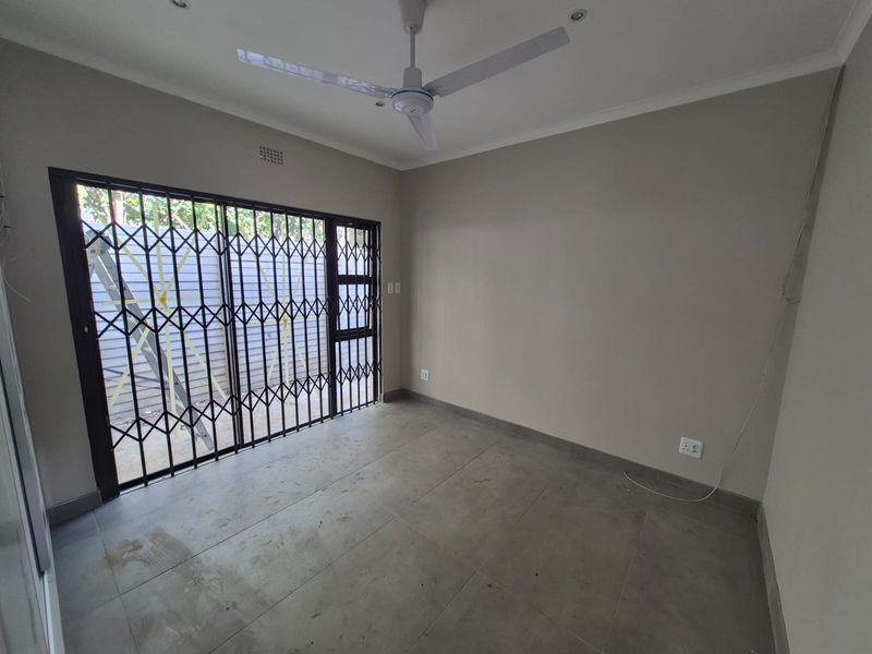 An empty living room featuring neutral walls, large format floor tiles, a ceiling fan, and a sliding door with a security gate.