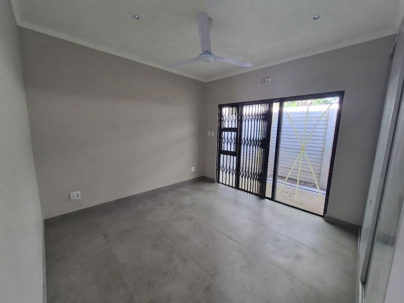 A clean, empty bedroom featuring neutral tiled flooring, a ceiling fan, and a sliding glass door with a security gate leading to the exterior.