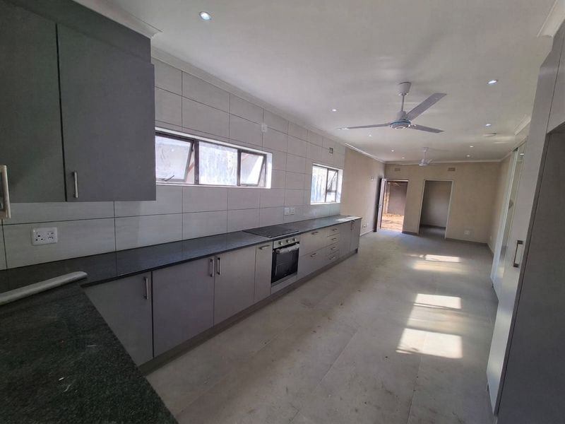 Spacious open-plan kitchen and living area featuring modern grey cabinetry, granite countertops, built-in oven, and sleek tiled flooring throughout.