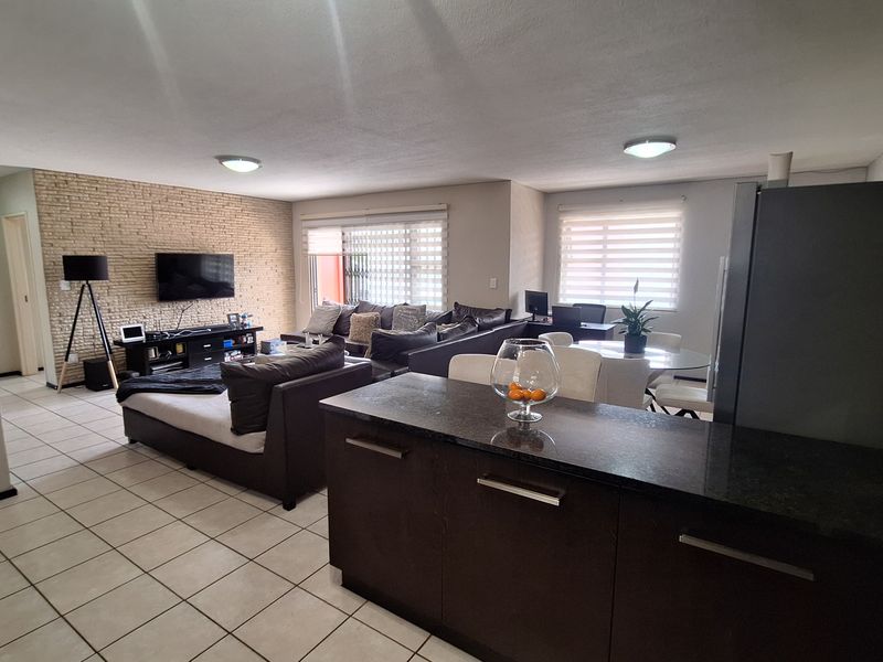 Spacious open-plan living area featuring tiled floors, an exposed brick feature wall, and a functional kitchen with dark cabinetry and granite countertops.