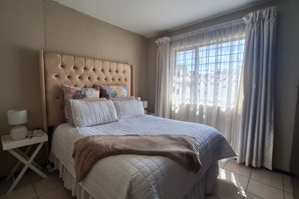 A bedroom featuring tiled flooring and a window fitted with security bars, providing natural light.