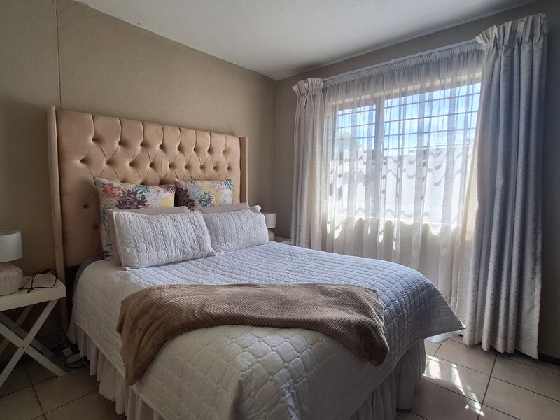 A bedroom featuring tiled flooring and a window fitted with security bars, providing natural light.