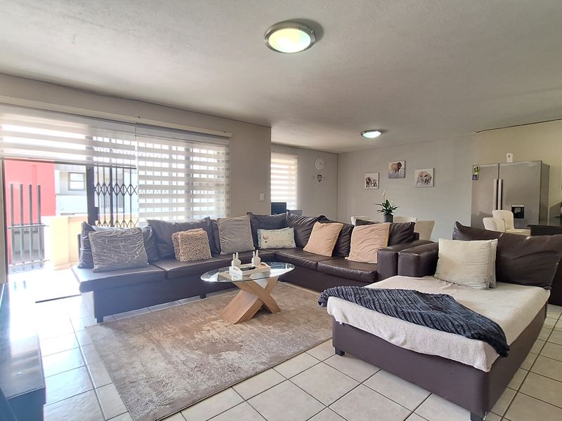 Spacious open-plan living area featuring tiled floors, an exposed brick wall, and direct access to a balcony through sliding glass doors.