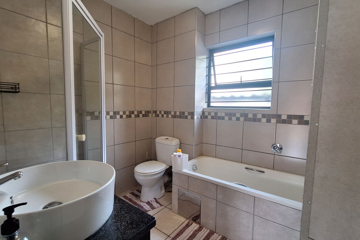 A well-maintained bathroom featuring a vessel sink on a granite vanity, a separate shower enclosure, a bathtub, and neutral wall tiling.