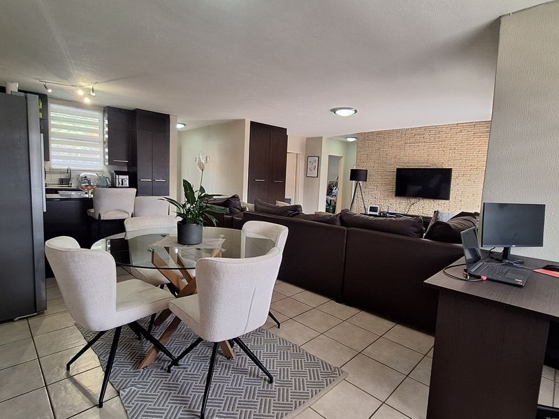 Spacious open-plan living area featuring a modern kitchen, dining space, and a distinctive brick feature wall, finished with neutral floor tiles throughout.