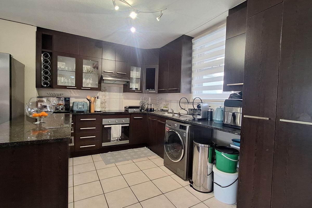 A functional kitchen featuring dark wood cabinetry, granite countertops, built-in oven, extractor fan, and tiled flooring with integrated laundry appliance space.