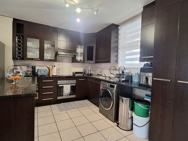 A functional kitchen featuring dark wood cabinetry, granite countertops, built-in oven, extractor fan, and tiled flooring with integrated laundry appliance space.