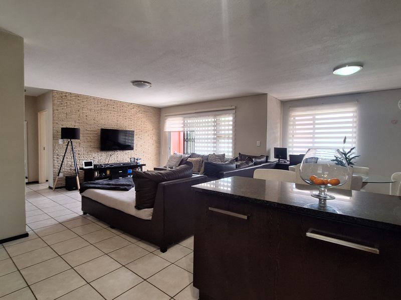 Spacious open-plan living area featuring tiled floors, a textured brick feature wall, and a modern kitchen with granite countertops and built-in cabinetry.