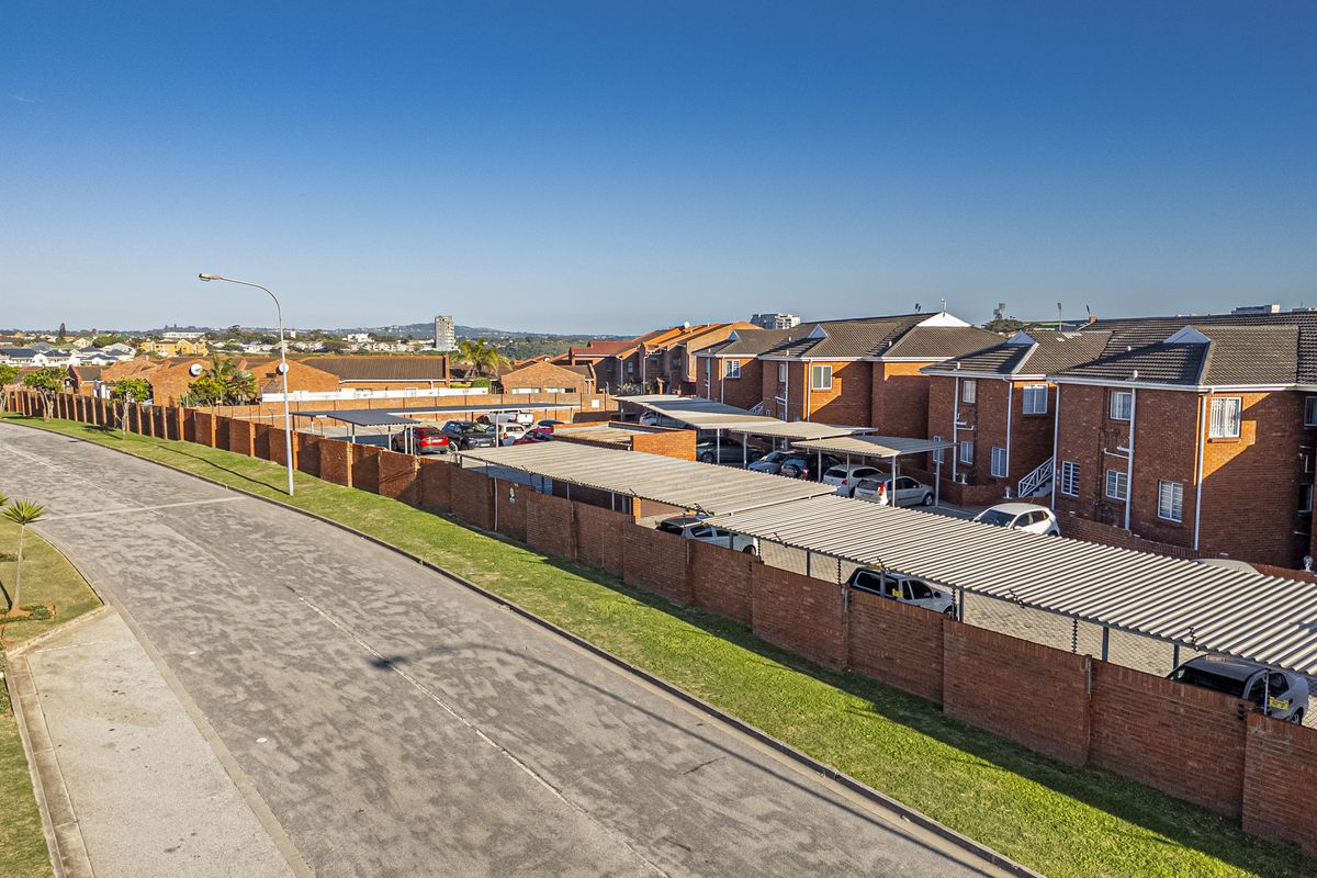 Aerial view of an apartment complex featuring brick buildings, tiled roofs, and covered parking bays within a secure perimeter wall.