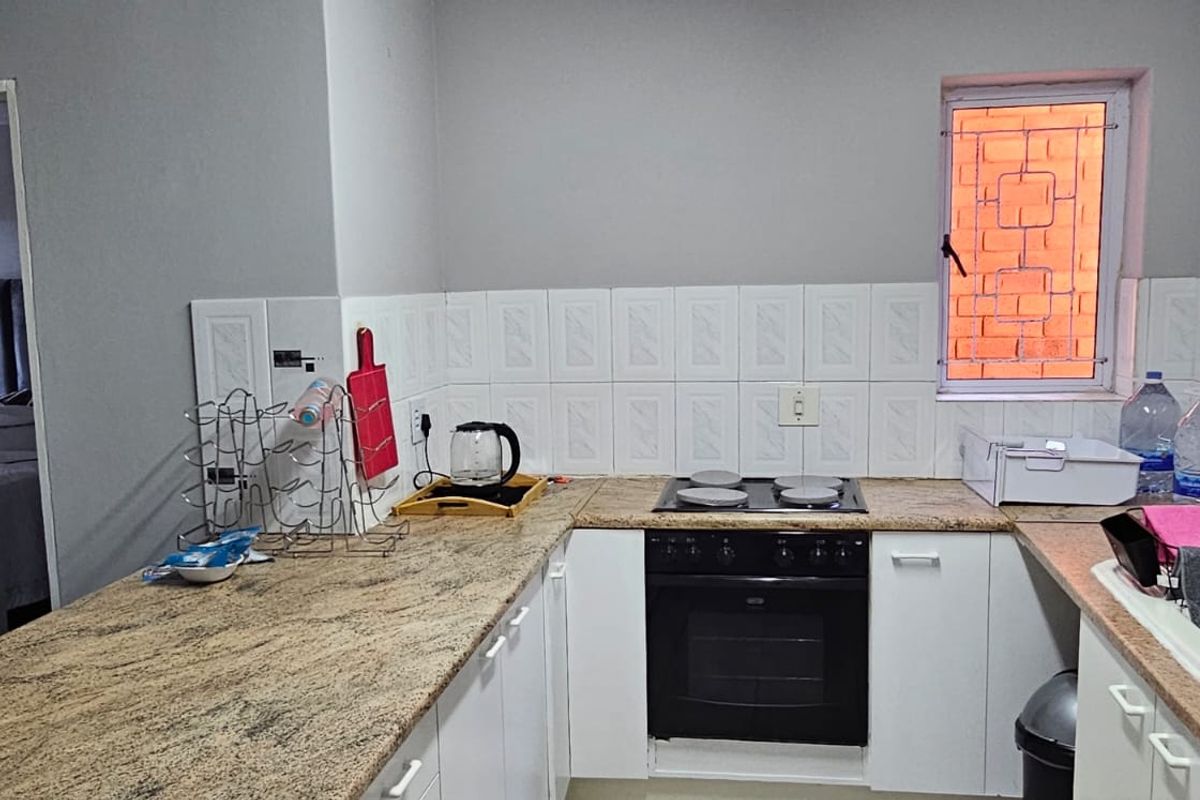 Functional kitchen featuring granite countertops, built-in cabinetry, and a built-in oven with electric hob, complemented by a tiled backsplash and security-fitted window.