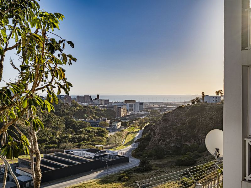 An elevated view overlooking the surrounding landscape, urban area, and distant coastline, captured from a balcony with a satellite dish.