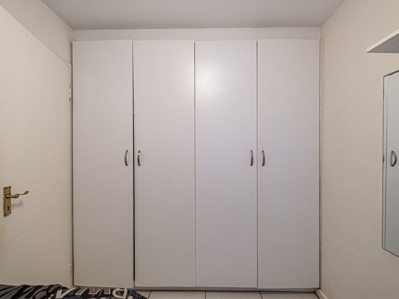 A bedroom featuring a white built-in wardrobe with four doors and tiled flooring.