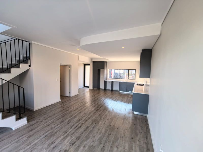 Modern open-plan living area featuring laminate flooring, a sleek kitchen with built-in cabinetry, and a contemporary staircase with a metal balustrade.