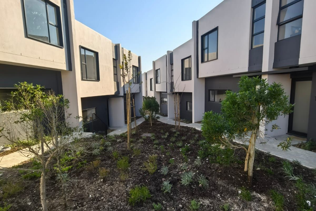 A view of the modern rear exterior facade of the residential complex, featuring clean architectural lines, paved pathways, and established garden landscaping.