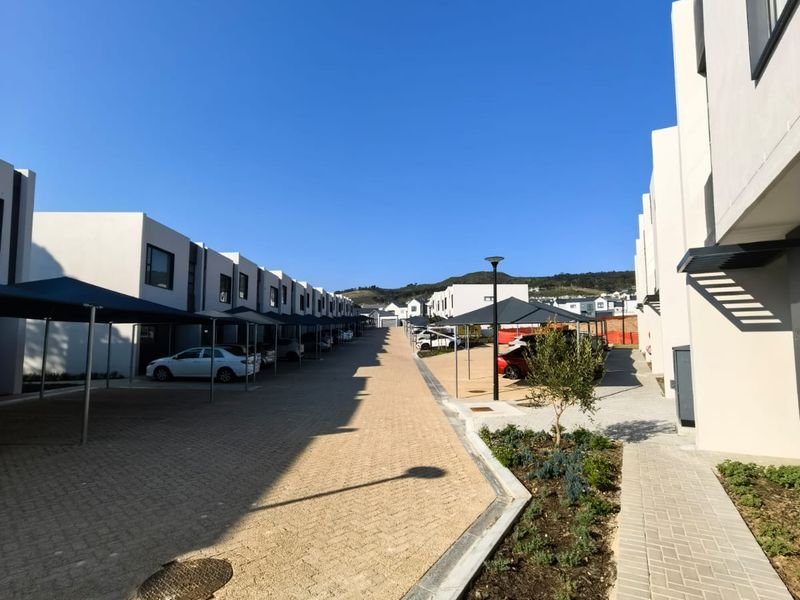 A well-maintained residential complex driveway featuring paved surfaces, covered parking bays, and neat landscaped garden borders under a clear sky.
