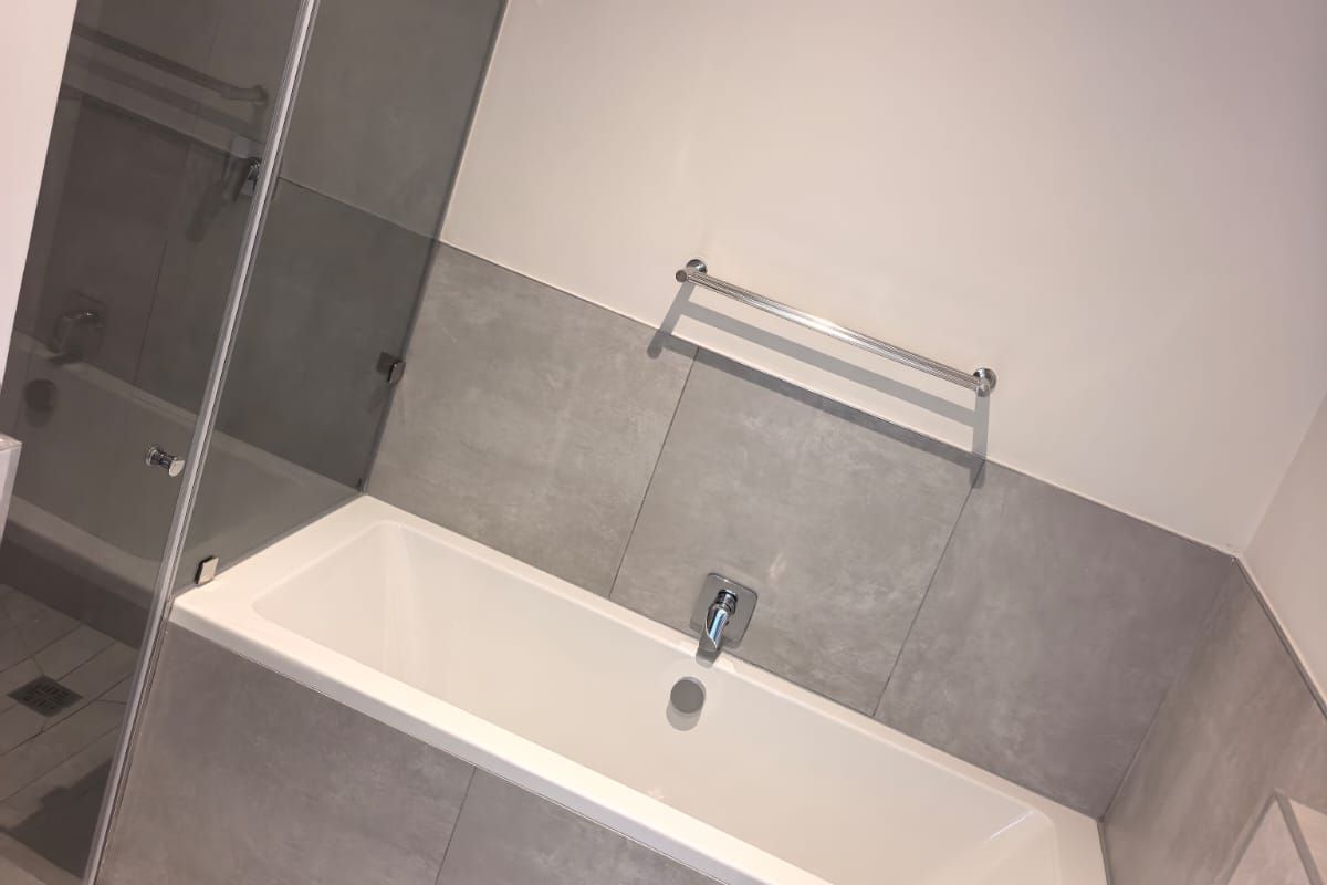 Modern bathroom featuring a built-in bathtub, glass shower enclosure, and neutral grey wall and floor tiling with chrome fixtures.