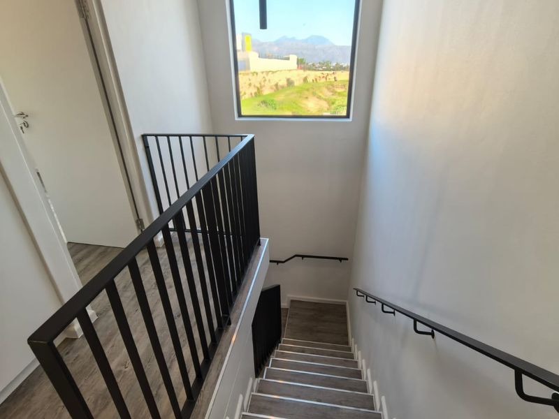 A modern, well-lit staircase featuring laminate wood-look flooring, a sleek black metal balustrade, and a large window offering scenic views.