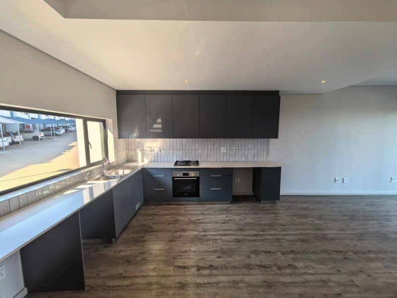 Modern kitchen featuring dark grey cabinetry, integrated oven, gas hob, and a tiled backsplash, set against a bright, open-plan living area.