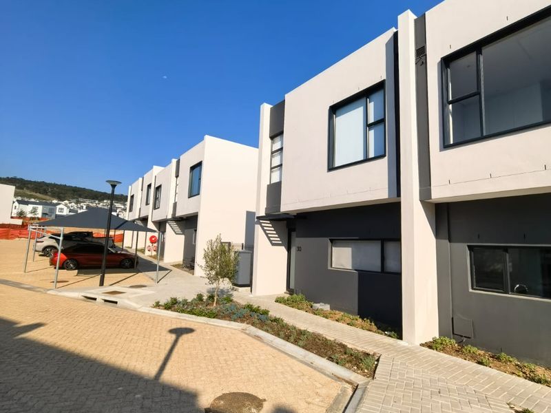 Modern multi-story residential townhouse exterior featuring clean architectural lines, paved driveway, and contemporary dark-framed windows in a well-maintained estate setting.