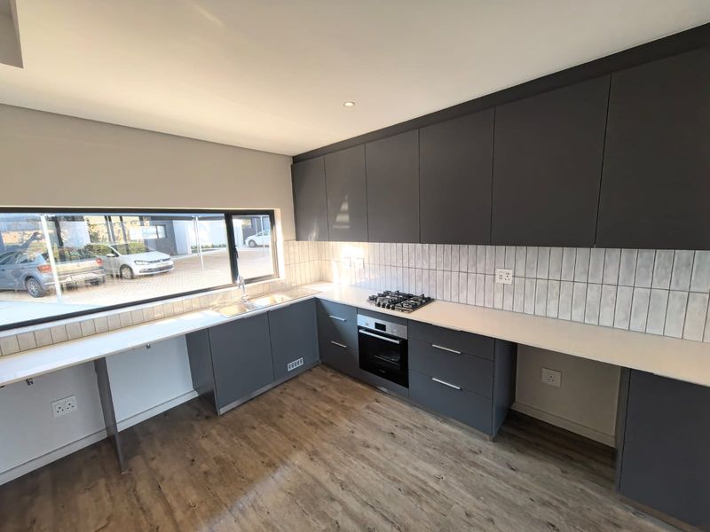 Modern kitchen featuring dark grey cabinetry, white countertops, integrated gas hob and oven, tiled backsplash, and wood-look laminate flooring.