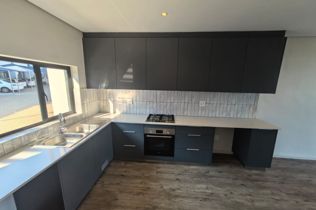 Modern kitchen featuring dark grey cabinetry, stone countertops, a gas hob, built-in oven, and a double sink with a tiled splashback.