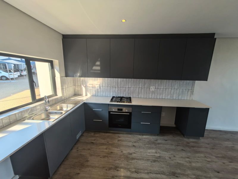 Modern kitchen featuring dark grey cabinetry, stone countertops, a gas hob, built-in oven, and a double sink with a tiled splashback.
