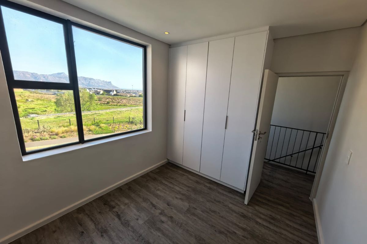 A bright, modern bedroom featuring built-in cupboards, laminate flooring, and large windows offering scenic mountain views.